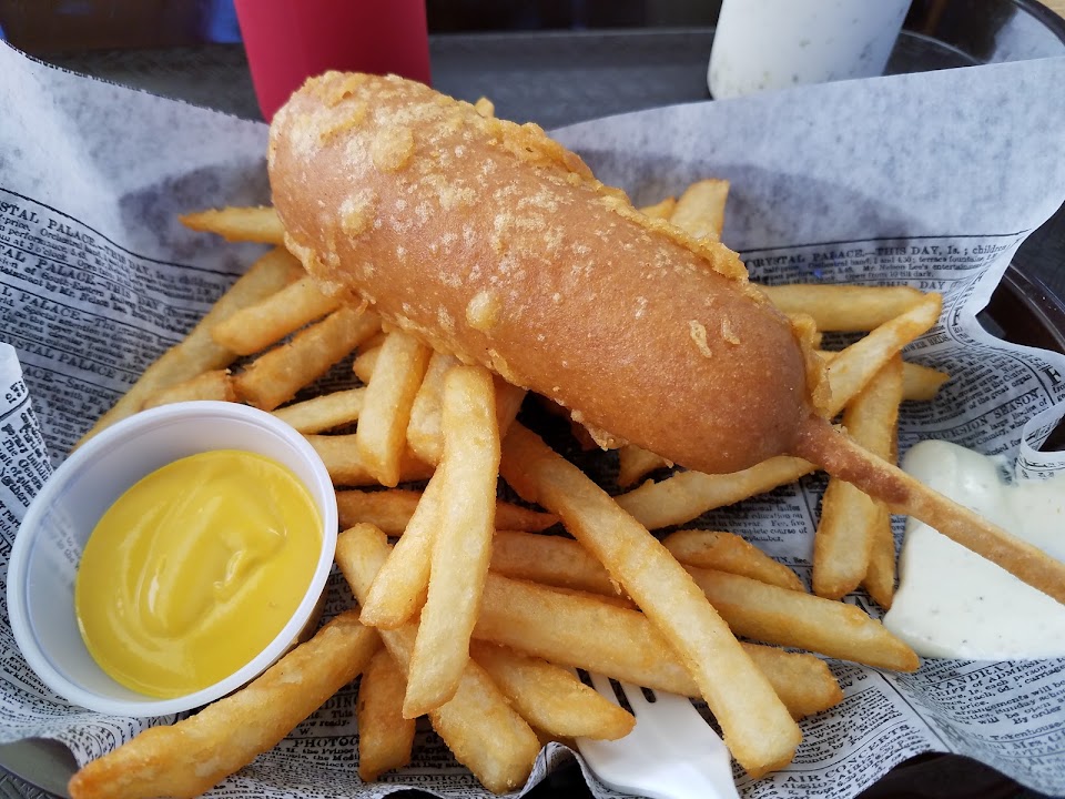 A golden battered fish fillet on a bed of fries with tartar sauce